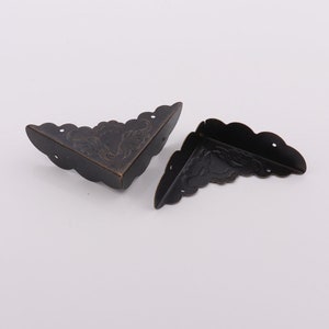 Puede incluir: Dos protectores de esquina de metal negro antiguo con un diseño floral decorativo. Los protectores de esquina están hechos de metal y tienen un acabado desgastado.