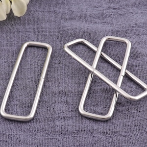 May include: Three silver metal D-rings, two are connected together and the third is separate. The rings are on a gray fabric background.