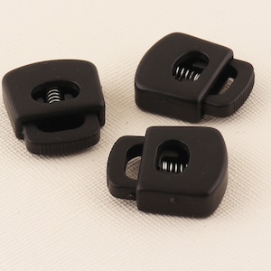 Puede incluir: Tres cierres de cordón de plástico negro con un mecanismo de resorte. Los cierres de cordón están diseñados para asegurar cordones o correas.