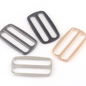 May include: Four metal slider buckles in different finishes: black, silver, gold, and rose gold. Each buckle has two parallel slots.