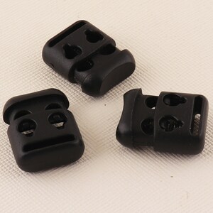 May include: Three black plastic cord locks with a rectangular shape and multiple holes.