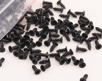 May include: A large quantity of black screws, scattered on a white surface. The screws have a Phillips head and are made of metal.