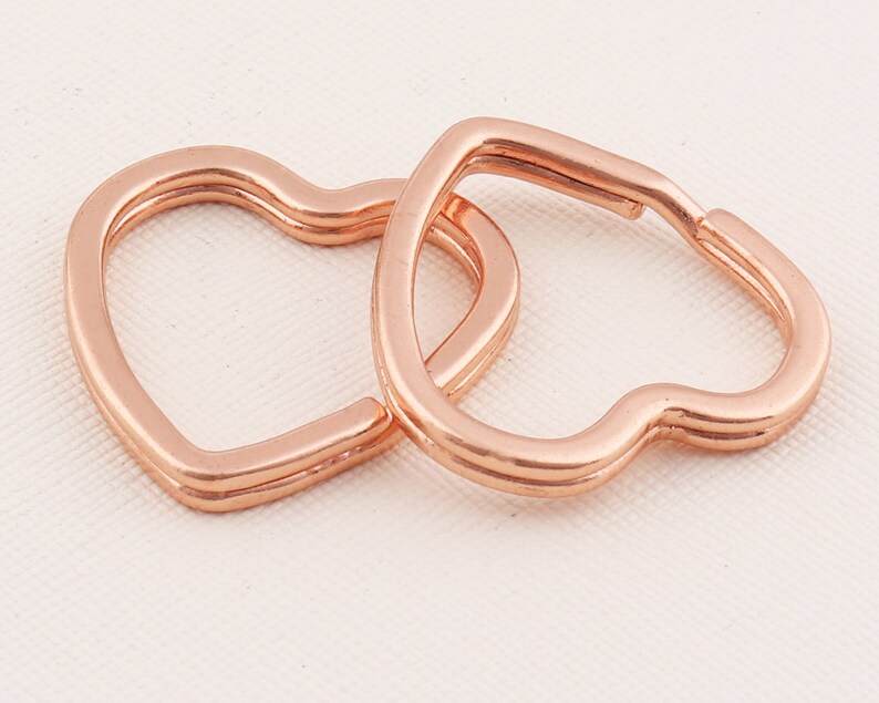 K&ouml;nnte beinhalten: Zwei herzf&ouml;rmige Schl&uuml;sselanh&auml;nger in Ros&eacute;gold. Die Schl&uuml;sselanh&auml;nger sind miteinander verbunden.