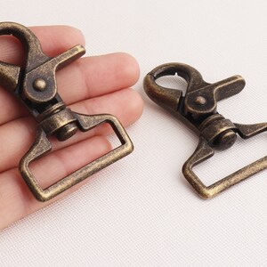 May include: Two antique gold-toned metal swivel clasps. The clasps are made of metal and have a rectangular shape with a hook on one end and a loop on the other.
