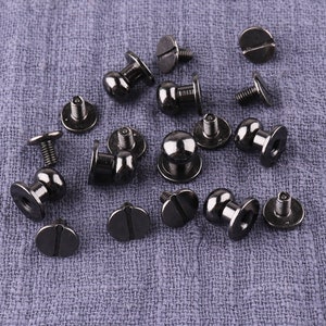 May include: A collection of 14 black metal screw-on studs with round heads. The studs are arranged on a gray fabric background.