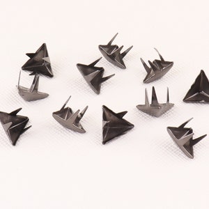 May include: A close-up of twelve silver triangle-shaped metal studs with three prongs on the bottom of each stud.