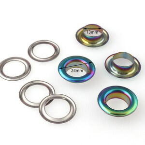 Op de afbeelding: Assortiment van metalen oogjes in verschillende maten, waaronder 13 mm en 24 mm. De oogjes hebben een regenboogkleurige, iriserende afwerking.