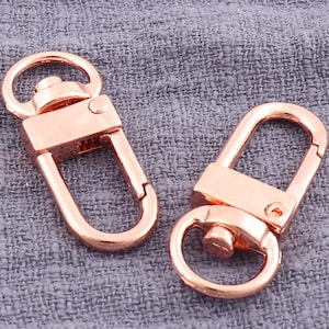 May include: Two rose gold metal swivel clasps. The clasps are oval shaped with a spring loaded gate.