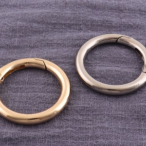 May include: Two metal key rings, one gold and one silver, on a gray fabric background.