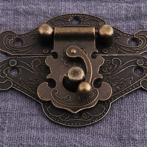 May include: Antique brass latch with an ornate floral design. The latch has two decorative knobs and a spring-loaded mechanism.