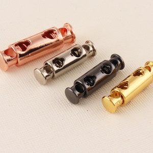 May include: Four cord stoppers in different colours: rose gold, silver, black, and gold. Each stopper has a spring mechanism and a heart-shaped design.