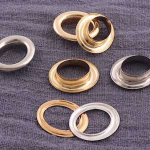 Könnte beinhalten: Sortiment an Metallösen in Gold- und Silberfarben. Die Ösen sind rund und haben ein Loch in der Mitte. Sie werden häufig für Bastelarbeiten, Kleidung und andere Projekte verwendet.