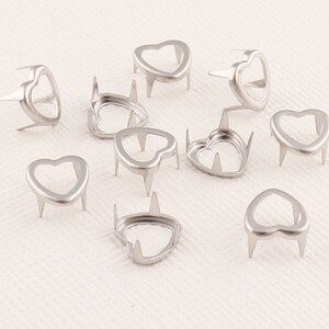 Puede incluir: Clavos de metal plateados en forma de corazón con puntas en la parte posterior. Estos clavos son ideales para agregar un toque de brillo a tus manualidades.