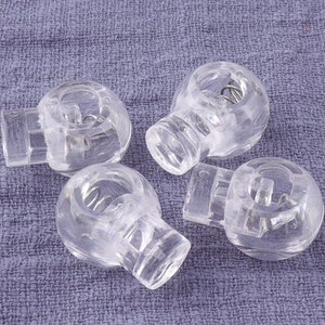 May include: Four clear plastic toggle clasps with a spring mechanism. The clasps are round and have a small hole in the center.