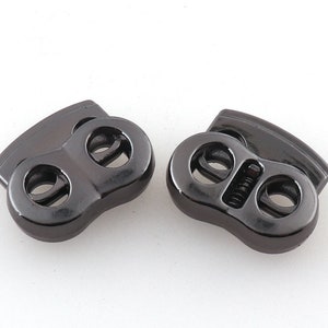 Puede incluir: Dos cierres de palanca de metal negro con dos agujeros cada uno. Los cierres están diseñados para usarse para ajustar la longitud de los cordones o correas.