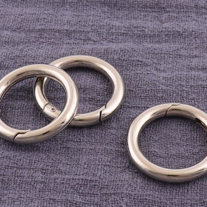 May include: Three silver metal key rings with a spring-loaded clasp. The key rings are on a gray fabric background.
