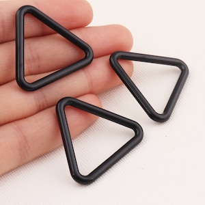 May include: Three black triangle-shaped metal rings. The rings are approximately 5 cm in diameter.