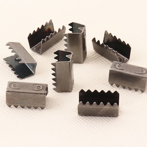 May include: A collection of eight dark gray metal picture frame hangers. Each hanger has a rectangular body with a series of jagged teeth on one side and a folded, slotted design on the other. The hangers are designed to securely hold picture frames.
