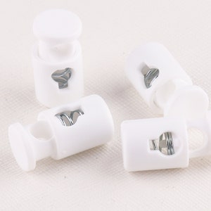 Puede incluir: Cinco cierres de cordón de plástico blanco con un resorte metálico en el interior. Los cierres de cordón se utilizan para asegurar cordones o correas.