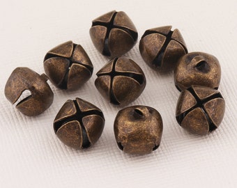 May include: A collection of ten antique gold-toned jingle bells with a cross-shaped design. The bells are arranged on a white surface.