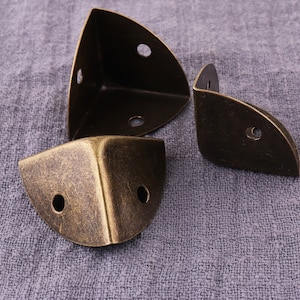 May include: Three antique brass corner brackets with a distressed finish. The brackets have three holes each for attaching to furniture.