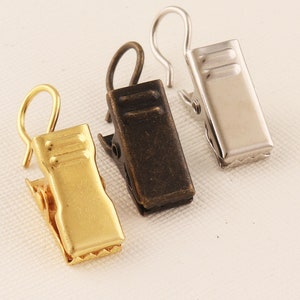 May include: Three curtain clips in gold, silver, and bronze finishes. Each clip has a hook at the top and a spring-loaded clip at the bottom.