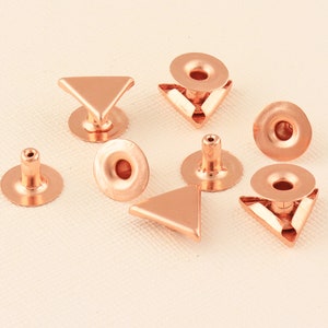 May include: A set of eight copper-colored metal rivets, including round and triangular shapes. The rivets have a decorative, vintage look and are ideal for adding a unique touch to leather goods, clothing, or craft projects.