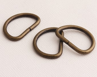 May include: Three antique gold-toned metal D-rings. The rings are interlocked, with one ring partially obscured by the other two.