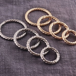 Könnte beinhalten: Ein Satz von sechs silbernen und goldenen Metallringen mit einem gedrehten Seil-Design. Die Ringe sind offen und haben einen Federschluss.