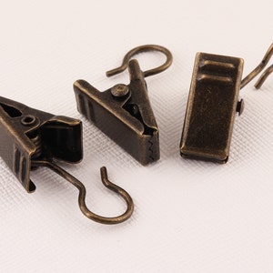 Puede incluir: Tres clips de cortina de oro antiguo con ganchos. Cada clip tiene un mecanismo de resorte para sujetar la tela.