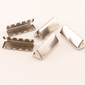 Peut inclure: Quatre embouts de sangle en métal argenté avec un bord dentelé. Les embouts de sangle sont conçus pour être utilisés pour fixer des sangles à du tissu.