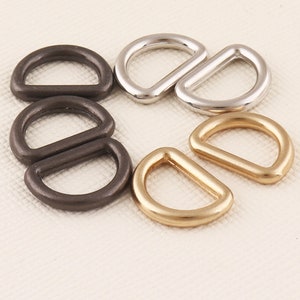 Puede incluir: Cinco anillos en D de metal en diferentes tamaños y acabados. Dos son plateados, dos son negros y uno es dorado.