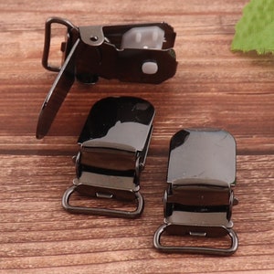 May include: Three black metal baby or toddler clothing clips. The clips have a shiny finish and are designed to be attached to clothing.