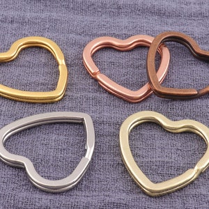 Op de afbeelding: Vier hartvormige sleutelhangers in verschillende kleuren: goud, zilver, koper en rosé goud. De sleutelhangers zijn gemaakt van metaal en hebben een gladde afwerking.