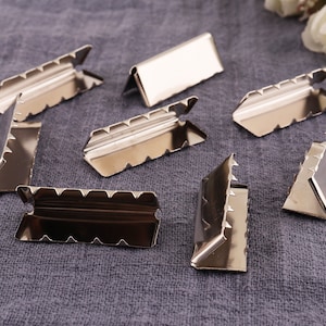 May include: Eight silver metal corner protectors with a scalloped edge. The protectors are designed to protect corners from damage.
