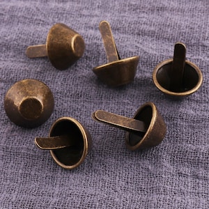 May include: Six antique gold-toned metal rivets with a domed head and a pointed shank. The rivets are arranged on a gray fabric background.