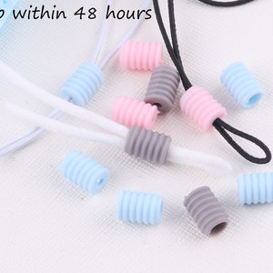 Peut inclure: Assortiment de bouchons de cordon en silicone de différentes couleurs, rose, bleu et gris. Les bouchons sont conçus pour empêcher les cordons de s'effilocher et sont parfaits pour une utilisation avec des masques faciaux, des écouteurs et d'autres cordons.