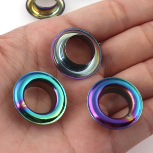 Op de afbeelding: Vier regenboogkleurige metalen oogjes met een rond gat in het midden. De oogjes hebben een regenboogkleurige afwerking.