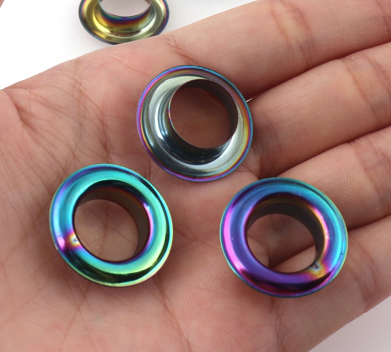 Op de afbeelding: Vier regenboogkleurige metalen oogjes met een rond gat in het midden. De oogjes hebben een regenboogkleurige afwerking.