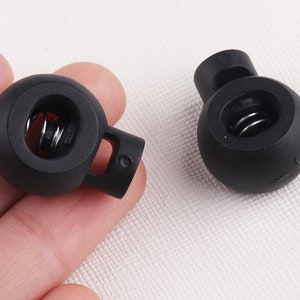 Puede incluir: Dos topes de plástico negro con un resorte en el interior. Los topes tienen un pequeño agujero en el lateral para sujetarlos a un cordón o cuerda.