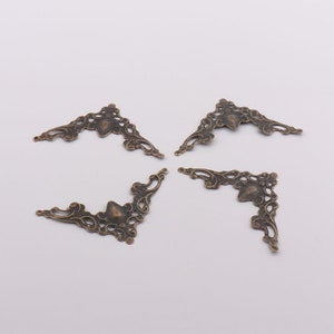 May include: Four antique gold corner brackets with a decorative floral design. The brackets are made of metal and have a distressed finish.