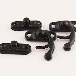 May include: Four black metal clasps with a hook and loop design. The clasps are designed to be used for fastening fabric or leather.
