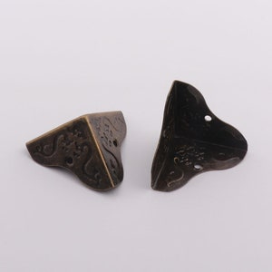 May include: Two antique gold corner protectors with an ornate design. The protectors are made of metal and have a distressed finish.