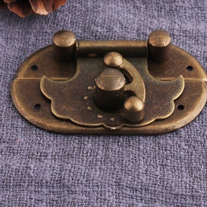 May include: Antique brass latch with a decorative design. The latch has a hinged lid and a locking mechanism.