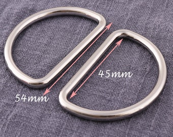 May include: Two silver metal D-rings, one measuring 54 mm and the other 45 mm. The rings are shown on a gray fabric background.