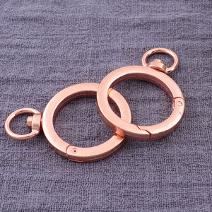 以下が含まれることがあります： 回転式留め具が付いた2つのローズゴールドの金属製キーリング。キーリングは互いに接続されています。