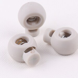 May include: Three gray plastic toggle stoppers with a metal spring inside. The stoppers have a round shape and a hole in the center.