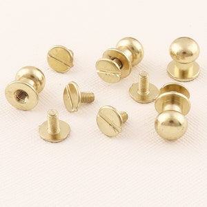 May include: Assortment of gold-toned metal screw-on fasteners with round heads and flat bases. Some fasteners have a slotted screw head, while others have a round head with a raised centre.
