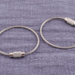 Pode incluir: Dois chaveiros de metal prateado com um design de cabo trançado e um fecho de barril prateado.