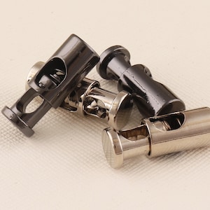 Puede incluir: Tres cierres de palanca metálicos en plata y negro. Los cierres se utilizan para ajustar la longitud de los cordones o correas.